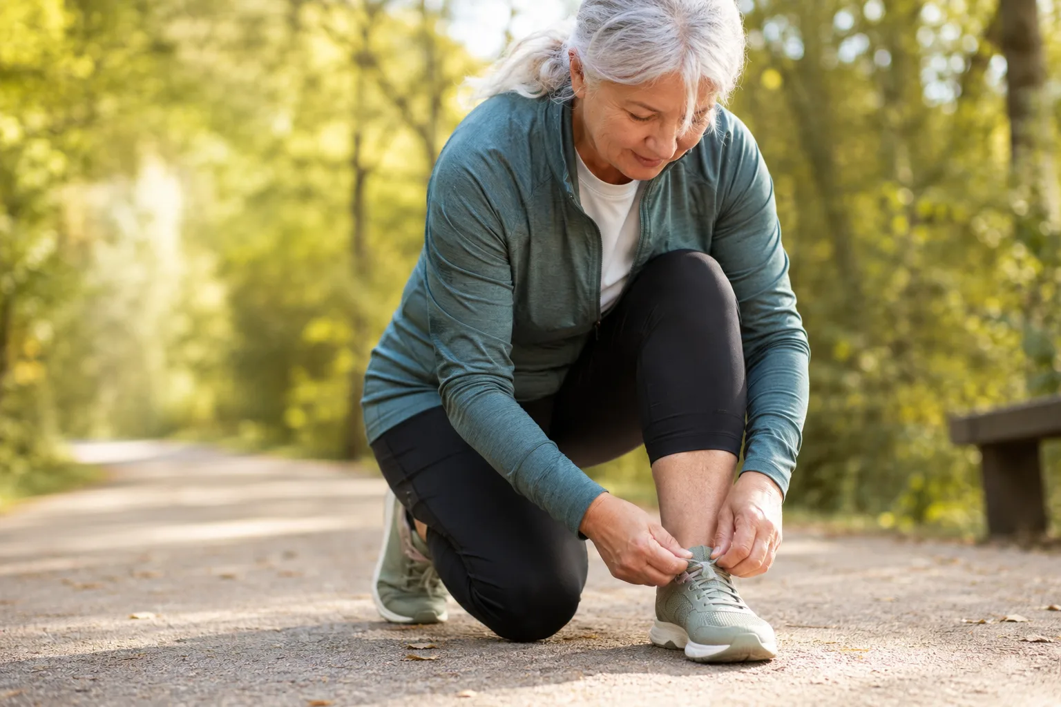 Mujer mayor atándose unas zapatillas deportivas antes de caminar por un parque