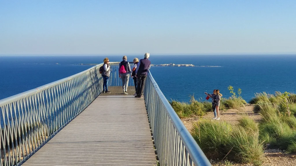 Grupo de viajeros mayores contemplando el mar desde un mirador costero.